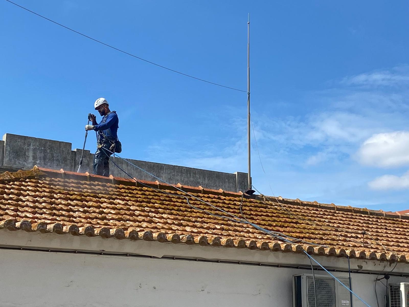 Trabalhador a limpar telhado com hidrolimpeza em altura